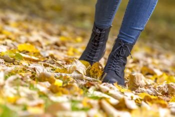 woman feet boots walking on fall leaves outdoor with autumn season nature on background
