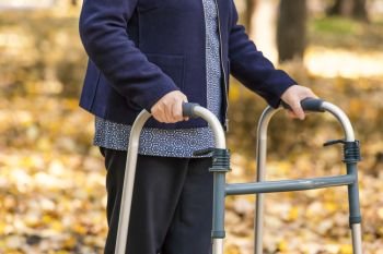 Closeup of senior woman legs walking with walker in autumn park. 
