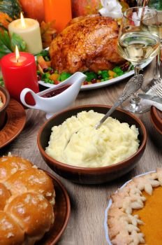 A bowl of mashed potatoes on a table among the pumpkin pie, baked turkey, cranberry-orange sauce,   a glass of white wine for Thanksgiving