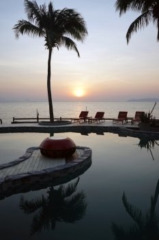 Chairs near pool with water and sea with sunset in Thailand