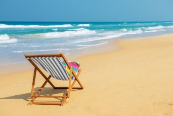 Deckchair with colorful bag on the beach near blue water side - vacation and travel concept.Striped deck chair on the sand.