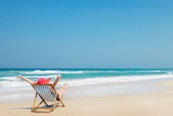 Happy woman  in red sunhat on the beach sitting on deckchair with hands up.Vacation and travel concept 