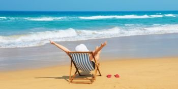 Happy woman  in white sunhat on the morning beach sitting on deckchair with hands up.Vacation and travel concept.