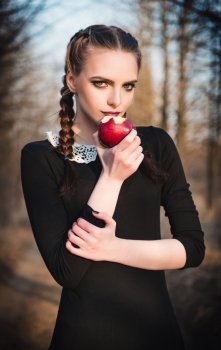 Outdoor portrait of a cute young girl in old-fashioned dress eating red apple