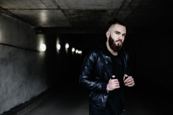 Modern young bearded man in black style clothes standing in around urban background.. Modern young bearded man in black style clothes standing in around urban background