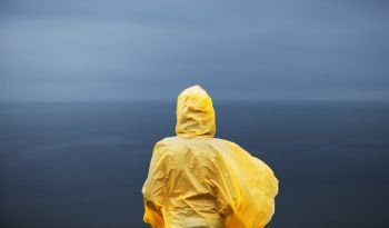 Woman in yellow raincoat looking away on deep blue sea in rainy autumn day.. Woman in yellow raincoat looking away on deep blue sea in rainy autumn day
