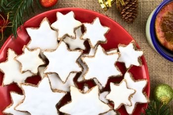 Traditional German Zimtsterne (cinnamon stars) Christmas cookies made of ground almonds, cinnamon, egg white and confectioner’s sugar, meringue on top, photographed overhead with Christmas decoration and mulled wine on the side. German Zimtsterne Christmas Cookies