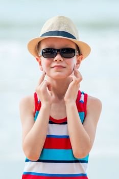Boy on the beach wearing a hat and glasses smears his skin with sunscreen