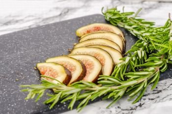 Fresh sliced figs and rosemary on cutting board