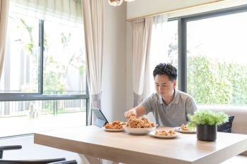 Young Asian man eating fried chicken in living room of contemporary house for modern lifestyle concept