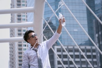 Asian Businessman standing and happy to drink water and hold bottle and modern city background
