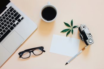 Creative flat lay photo of workspace desk with laptop, coffee, blank paper and film camera with copy space background, minimal styled