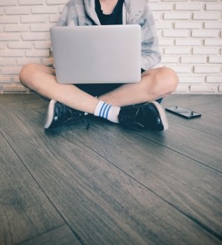 Young man using laptop and sitting on the floor in the cafe or home 