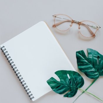 Flat lay of minimal workspace desk with notebook, eyeglasses and green plant, copy space