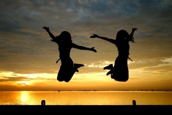silhouette of women jumping at the sea with beautiful sunset background
