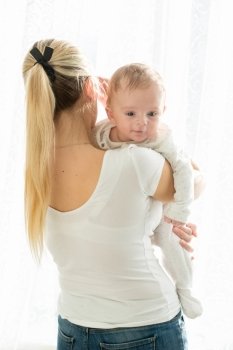Portrait of beautiful young woman with her 3 months old baby boy at big window