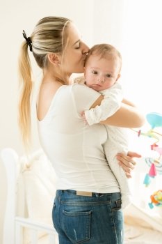 Portrait of beautiful mother hugging her adorable baby in bedroom at bright sunny day