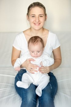 Beautiful smiling woman sitting at bedroom and holding her cute baby on laps