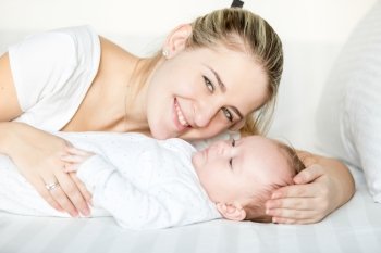 Closeup portrait of smiling mother lying with 3 months old baby on bed