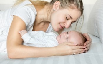 Closeup portrait of beautiful young mother cuddling her baby boy on bed