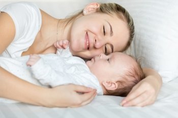 Closeup portrait of beautiful smiling woman lying with her cute baby on pillow at bed
