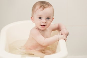 Toned portrait of lovely baby boy taking bath with foam
