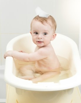 Cheerful baby boy playing in foam while having bath