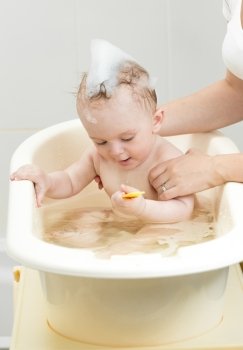 Portrait of lovely baby boy taking bath with foam
