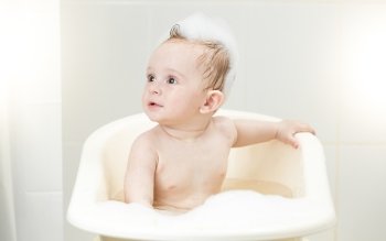 Cute baby boy sitting in foam at bathroom