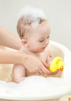 Portrait of cute baby boy playing in foam bath with yellow rubber duck