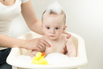 Portrait of cute baby boy playing with yellow rubber duck in bath