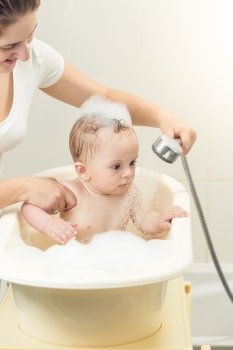 Portrait of cute baby boy playing in bath with shower head