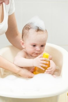 Portrait of cute baby boy having bath and holding shampoo bottle
