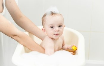 Young mother bathing her baby boy in plastic bath