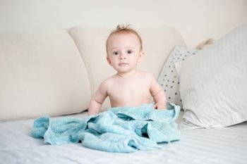 Happy 9 months old baby boy sitting on bed after bathing