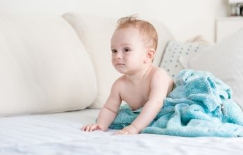 Adorable baby boy after shower covered in blue blanket on sofa at living room
