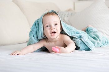 Portrait of happy smiling baby under blue towel crawling on bed with white sheets