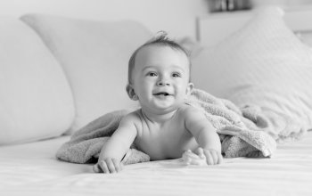 Black and white portrait of cheerful laughing baby boy lying under blanket on sofa