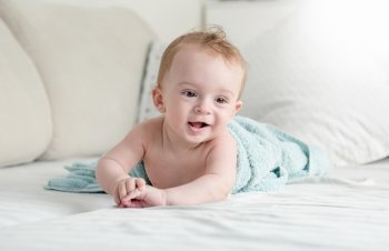 Beautiful 9 months old baby boy under blue towel lying on sofa at living room