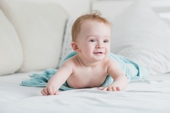 Portrait of adorable smiling baby in blue towel after shower crawling on bed