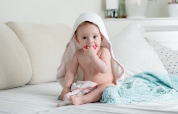 Adorable 9 months old baby boy sitting on bed under towel