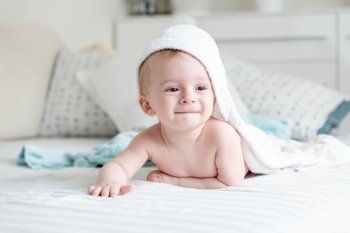 Cute smiling baby boy in hooded towel crawling on bed after having bath