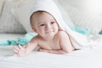 Happy 9 months old baby lying under white towel on bed