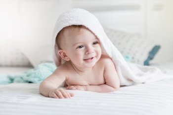 Portrait of adorable smiling baby in hooded towel ling on bed after having bathtime