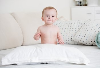Cute naked baby boy sitting on bed at bedroom