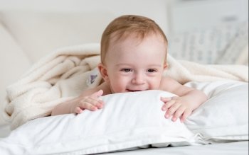 Portrait of cheerful smiling baby boy relaxing on big white pillow on bed