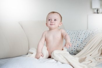 Adorable smiling baby boy in diapers sitting on bed with white sheets