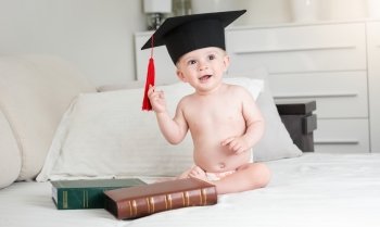 Portrait of funny baby boy in diapers wearing black graduation cap