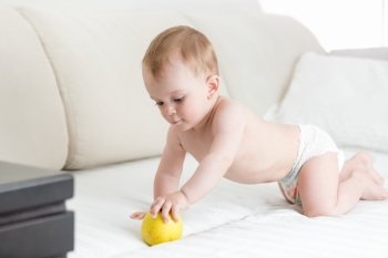 Adorable baby boy crawling on bed and reaching for apple