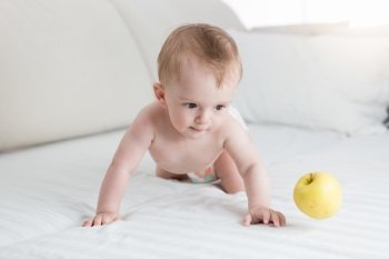Cute 10 months old baby boy playing with yellow apple on bed